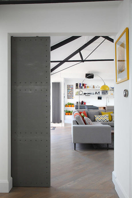 Modern living room interior with exposed beams and colorful decor seen through an open door.