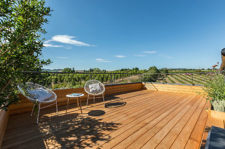 Wooden deck with two chairs overlooking vineyards under a clear sky.