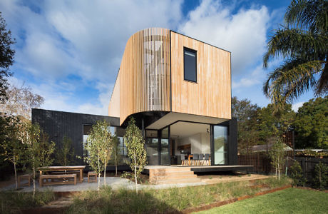 Modern house with wooden and black façade, large windows, and garden.