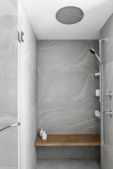 Minimalist grey tiled shower with wooden bench and rain showerhead.
