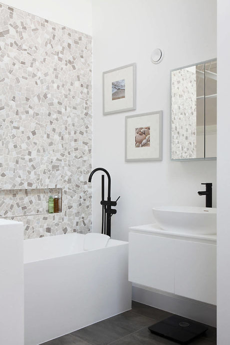 Modern bathroom with mosaic tile wall, white sink, and black faucet.