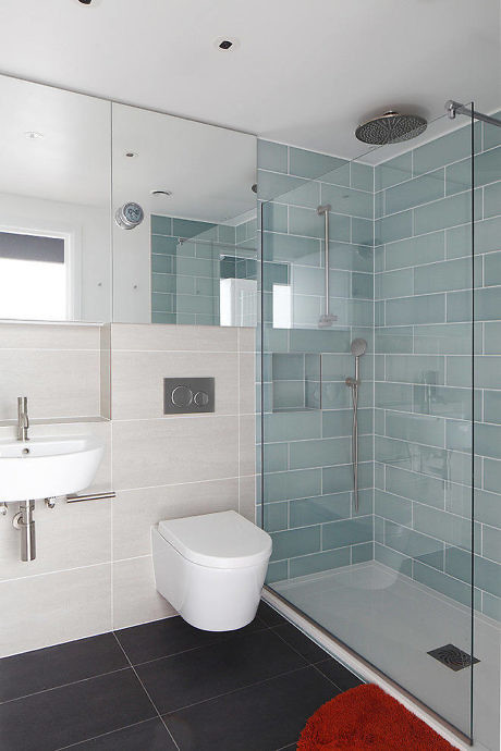Contemporary bathroom with blue tiled shower and sleek white fixtures.