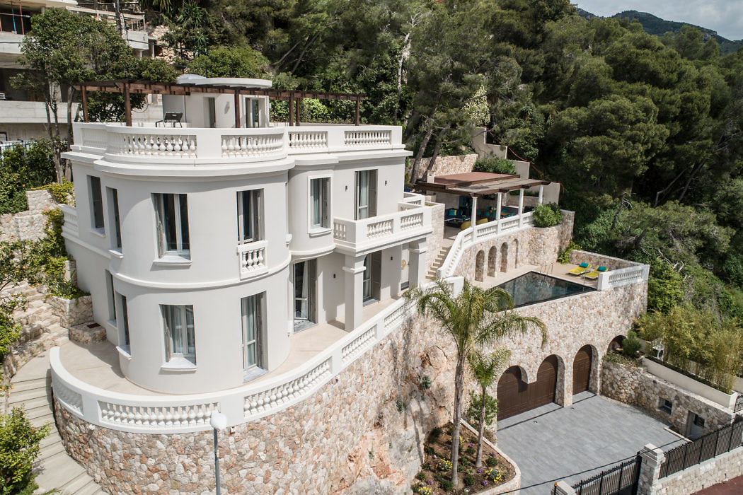 Elegant white villa with balconies, nestled on a lush hillside.