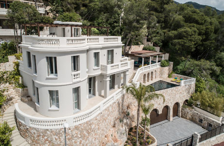 Elegant white villa with balconies, nestled on a lush hillside.