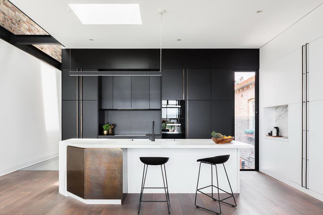 Sleek kitchen with black cabinetry, white countertops, and rustic wooden floors