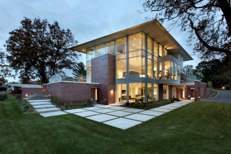 Modern two-story house with glass walls and brick accents at dusk.