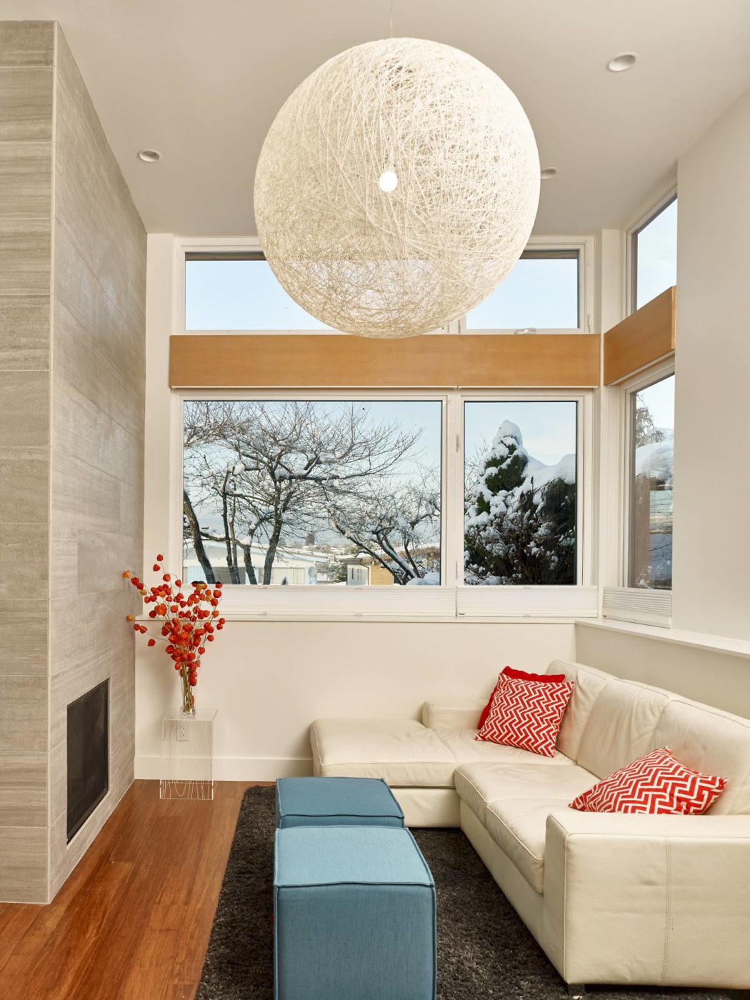 Modern living room with large pendant light, sectional sofa, and winter view through windows