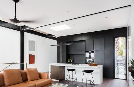Modern kitchen with black cabinetry and white countertops, adjacent to a living area with