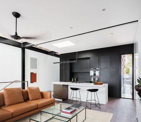 Modern kitchen with black cabinetry and white countertops, adjacent to a living area with