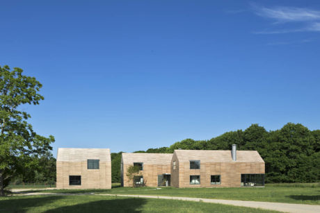 Modern cubic buildings with wooden facade in a grassy field under blue sky.