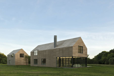 Modern house with gabled roofs and large glass windows on grassy terrain.