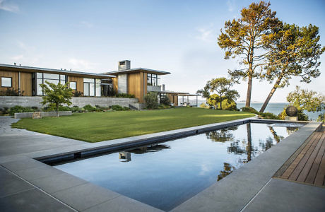 Modern house with large windows, reflecting pool, and ocean view.