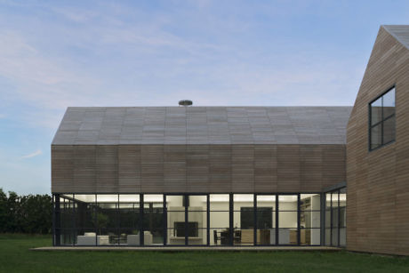 Modern house with large glass windows and wooden siding at dusk.