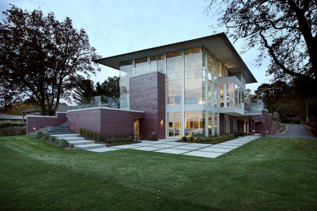 Modern two-story house with large glass windows and brick exterior at dusk.