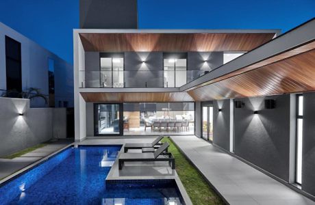 Modern house with illuminated interior, pool, and wooden accents at dusk.