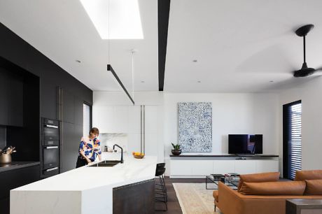 Modern kitchen interior with integrated living space and a person cooking.