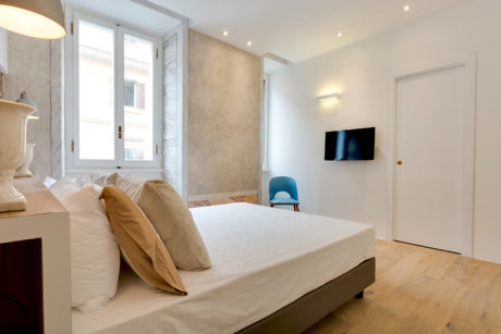 Modern bedroom with a white bed, wooden floor, and a TV on the wall