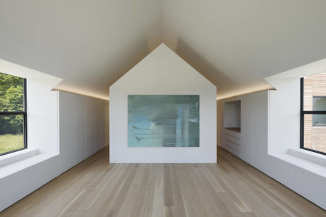 Minimalist attic room with gabled wall art, windows, and wooden floor.