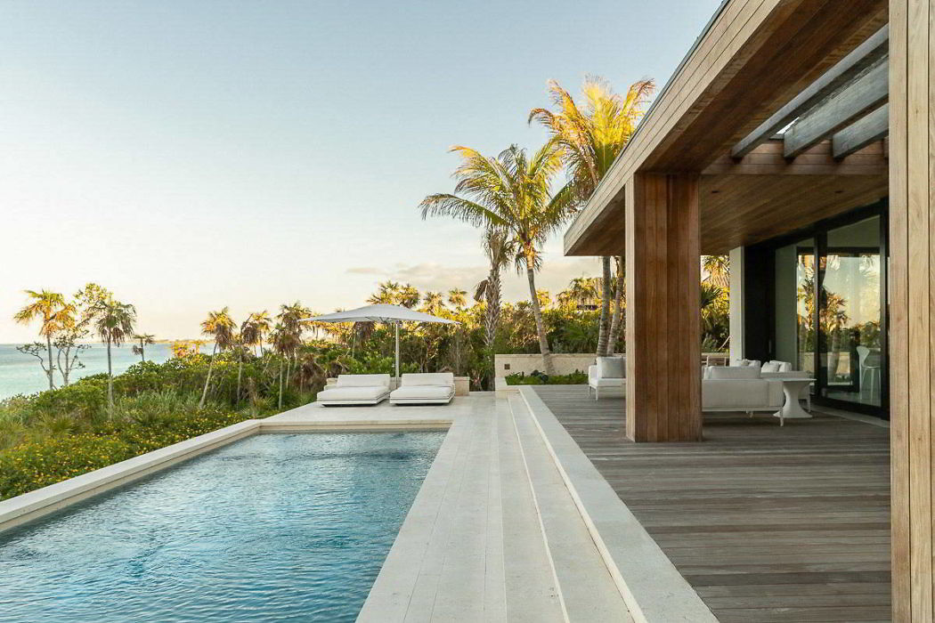 Modern beach house exterior with infinity pool and wooden deck.