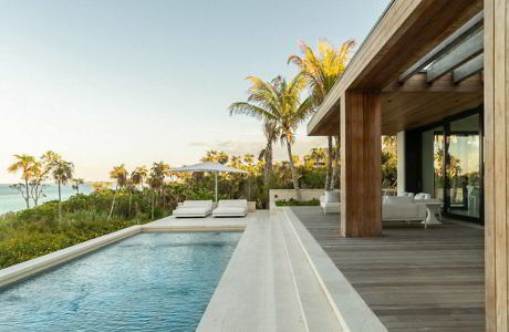 Modern beach house exterior with infinity pool and wooden deck.