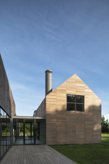 Modern gabled building with wood siding and large chimney against a blue sky.