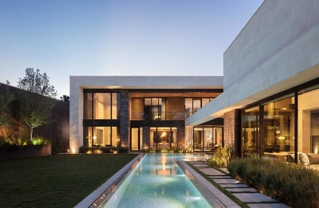 Modern two-story house with large windows, a central pool, and garden at dusk