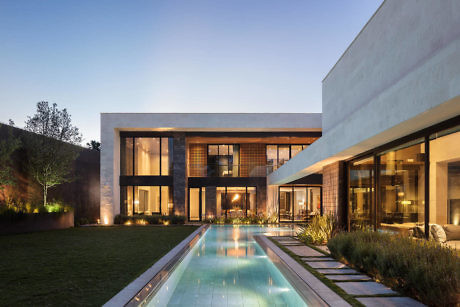 Modern two-story house with large windows, a central pool, and garden at dusk