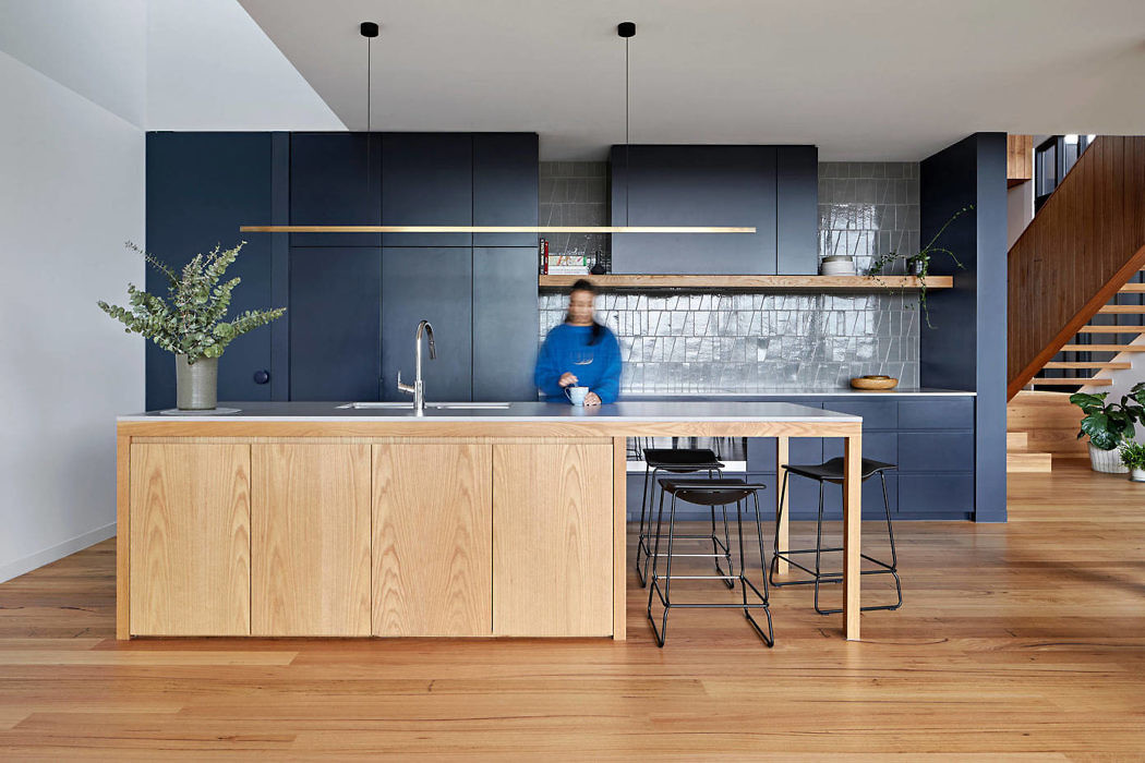 Modern kitchen with blue cabinets, wooden island, and a person sitting on a stool