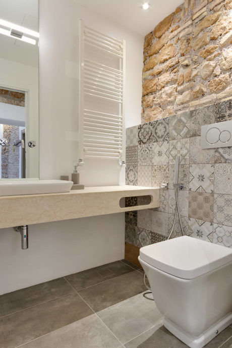 Modern bathroom with patterned tiles and exposed stone wall.