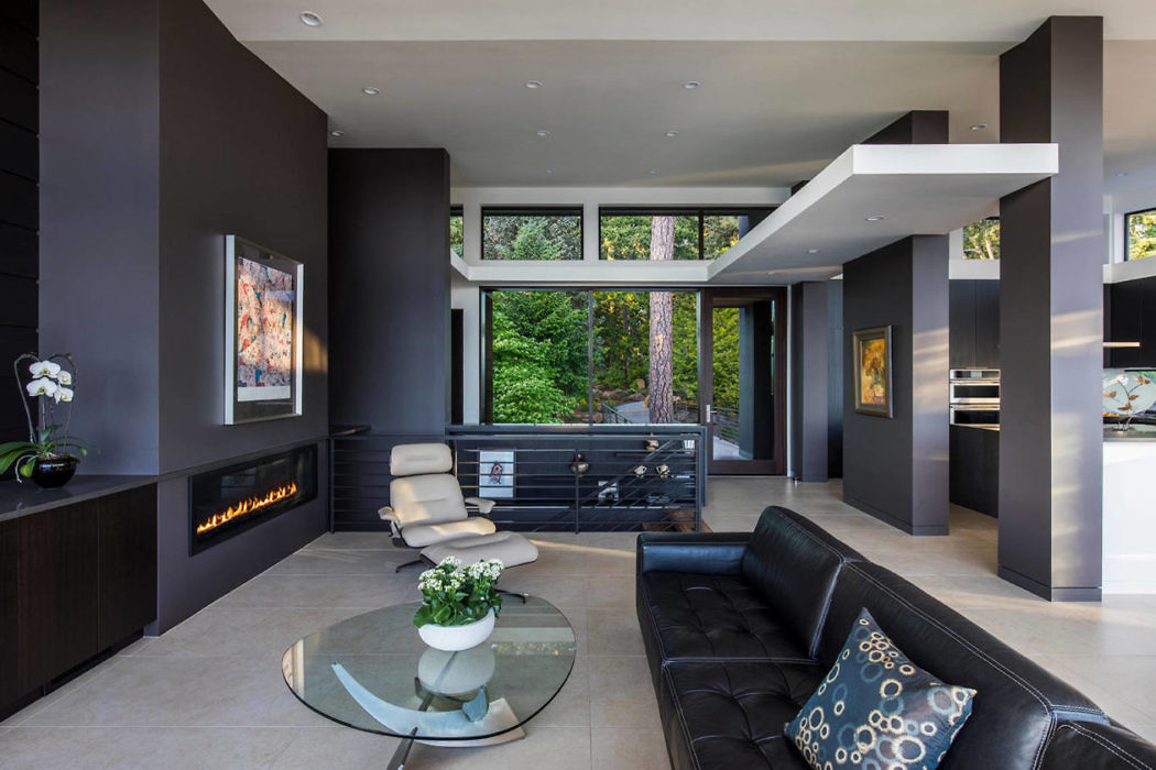Modern living room with dark walls, fireplace, leather furniture, and large windows.