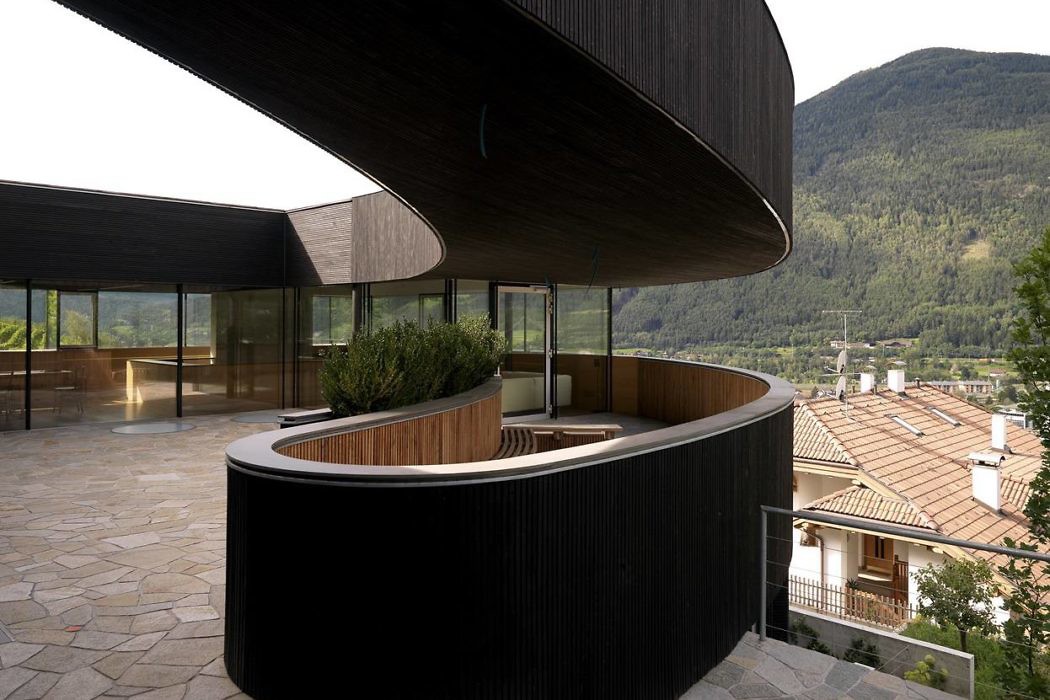 Curved building facade with wooden details overlooking mountains.