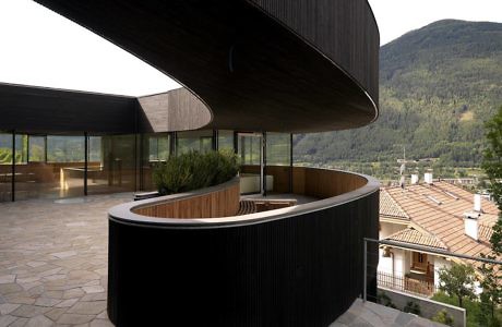 Curved building facade with wooden details overlooking mountains.