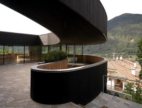 Curved building facade with wooden details overlooking mountains.
