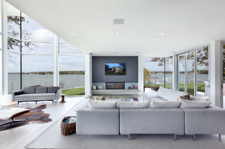 Modern living room with large windows overlooking a lake, minimalist furniture, and a central