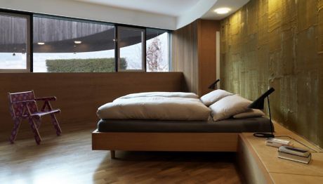 Modern bedroom with large bed, wooden floor, and gold accent wall.
