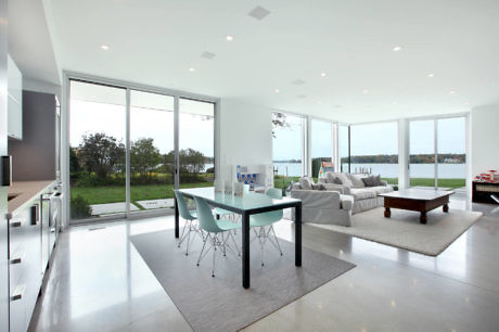 Modern living room with large windows overlooking a lawn and body of water.