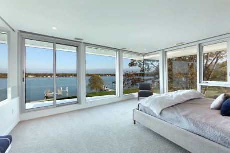 Modern bedroom with large windows overlooking a serene lake.