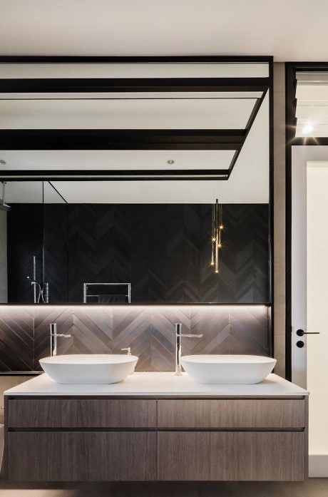 Modern bathroom vanity with two sinks, dark tiled wall, and large mirror.
