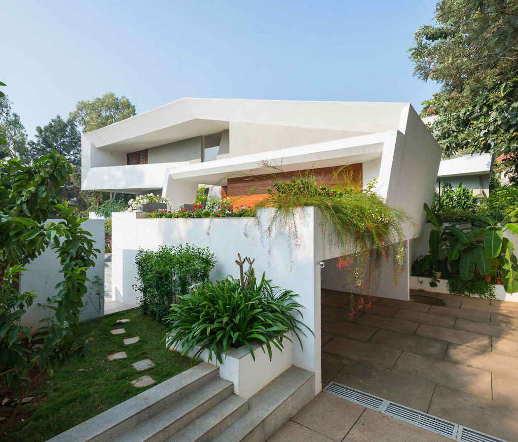 Modern white architect-designed house with angular shapes surrounded by greenery.