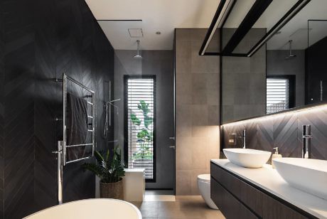 Modern bathroom with dark tiles, two vessel sinks, and a shower area.