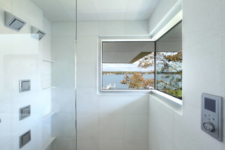 Minimalist white bathroom with a large window overlooking a scenic lake view.