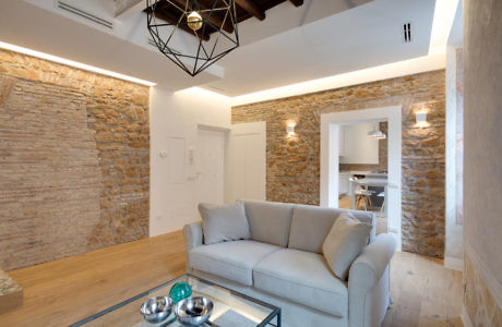 Modern living room with exposed stone walls and a geometric ceiling light.