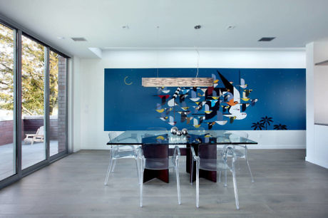 Modern dining room with a blue mural, glass table, and clear chairs.