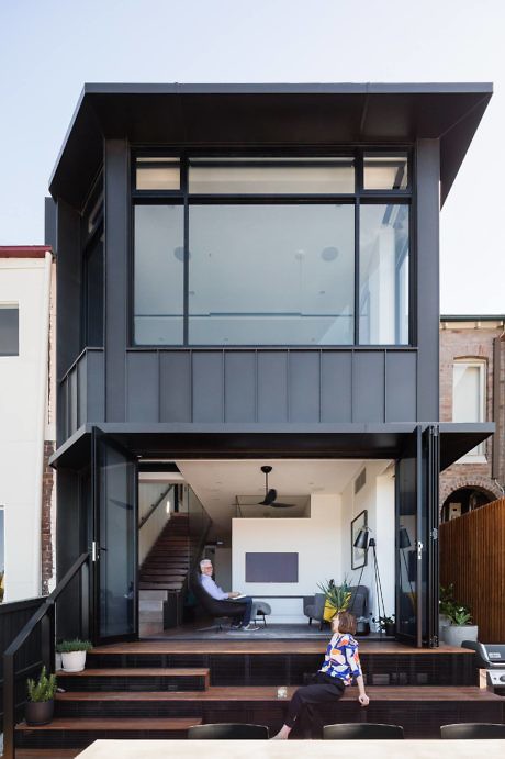 Modern two-story home extension with large windows and people in the interior space.