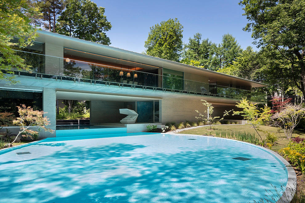 Modern glass house with reflective pool and lush greenery.