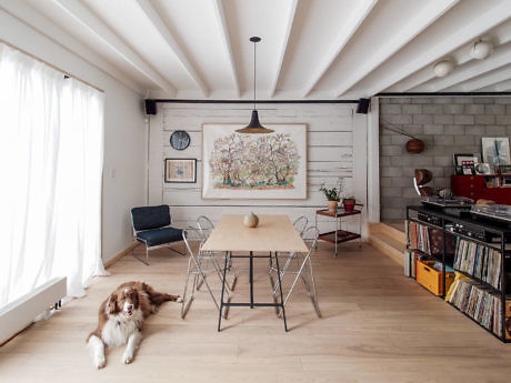 A rustic dining area with a floral wall art, wooden ceiling beams, and a canine companion.