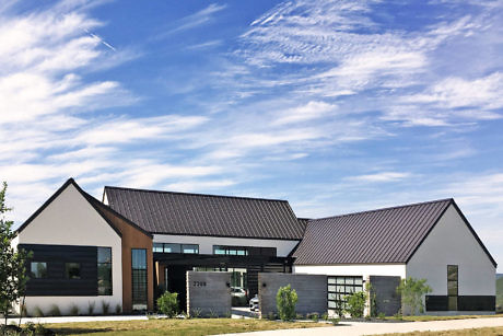 Modern building with steep black metal roofs, large windows, and landscaped yard.