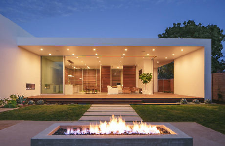 Minimalist, contemporary home with wood exterior, glass walls, and a fire pit feature.