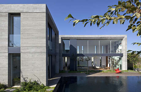 A modern, concrete residential building with glass walls and a water feature in the foreground.