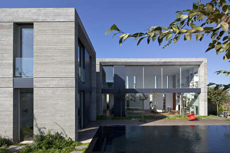 A modern, concrete residential building with glass walls and a water feature in the foreground.